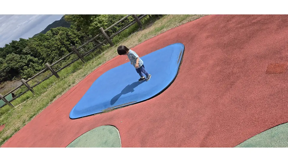 公園の大きな遊具の青い部分に立つ息子の後ろ姿